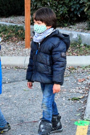 A kindergarten student playing outside with his friends. Face coverings and social distancing is required.